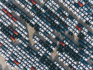 Open finished car warehouse of giant plant with rows of multi-coloured vehicles casting shadows in sunny summer morning aerial view