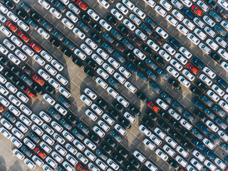 Open finished car warehouse of giant plant with rows of multi-coloured vehicles casting shadows in...