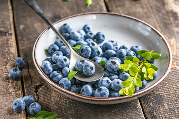 Freshly picked blueberries in a  bowl. Juicy and fresh berries with green leaves on a rustic table.  Healthy food and nutrition concept