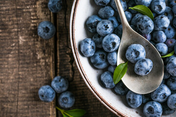 Freshly picked blueberries in a  bowl. Juicy and fresh berries with green leaves on a rustic table.  Healthy food and nutrition concept