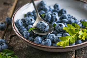 Freshly picked blueberries in a  bowl. Juicy and fresh berries with green leaves on a rustic table.  Healthy food and nutrition concept