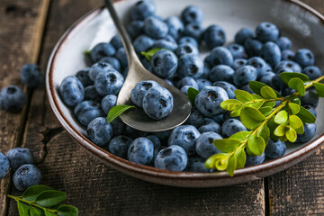 Freshly picked blueberries in a  bowl. Juicy and fresh berries with green leaves on a rustic table.  Healthy food and nutrition concept