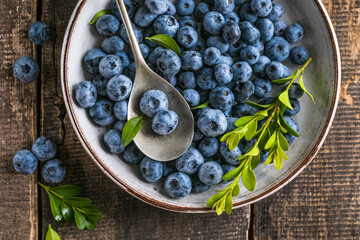 Freshly picked blueberries in a  bowl. Juicy and fresh berries with green leaves on a rustic table....