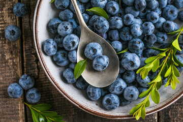 Freshly picked blueberries in a  bowl. Juicy and fresh berries with green leaves on a rustic table.  Healthy food and nutrition concept