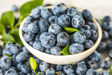 Freshly picked blueberries in a  bowl. Juicy and fresh berries with green leaves on a rustic table.  Healthy food and nutrition concept