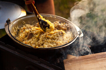 The female hand of the cook is stirring the pilaf with a spoon.