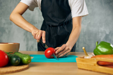Cook in black apron on the kitchen cutting vegetables salad diet