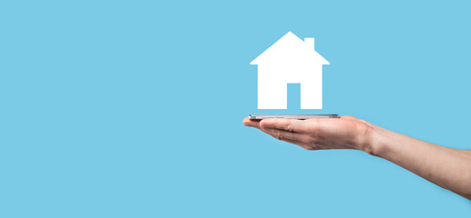 Male hand holding house icon on blue background. Property insurance and security concept.Real estate concept.Banner with copy space.