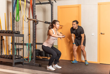 Young woman doing squats without weighting exercise with trainer in gym