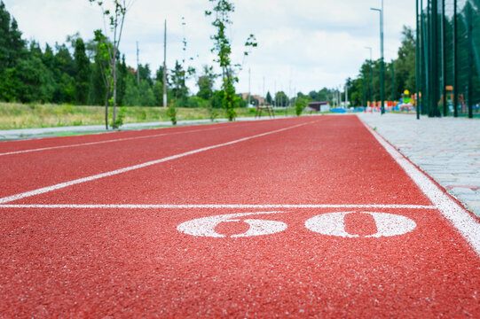 "60" mark on running track in the sport stadium. Sign in white numbers and line marked on a red rubber coating.