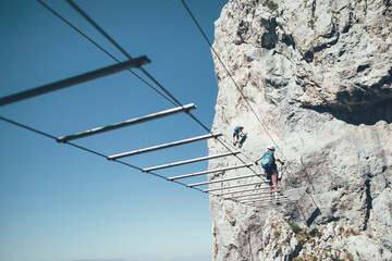 Two women climbers moving up and crossing wire bridge on via ferrata route