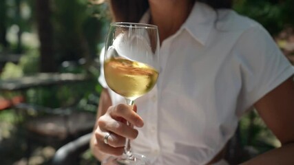 A woman holds a glass of white wine in a bar at the resort. Tourists test the concept of wine