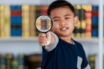 Circle magnifying glass tightly grab by genius Asian boy for studying funny knowledge of scientific observation, physic research, light, lens, image enlargement in library of elementary school