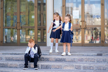 Two little schoolgirls tease a boy with red hair. A student sits on the stairs next to the school...