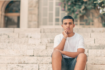 Portrait Of Male Teenage Student Sitting On The Stairs College Campus.