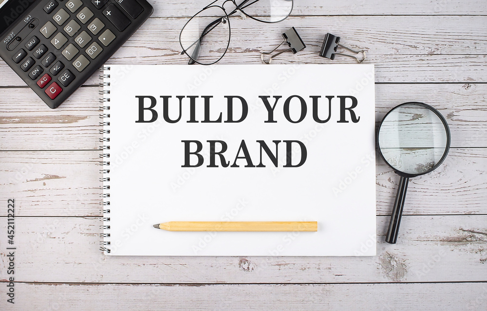 Poster blank notebook with text build your brand on white background with calculator and office tools.