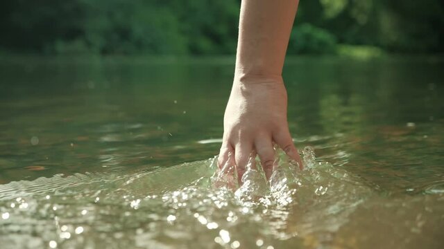 Slow motion of hand touching water stream river or lake flowing in the deep green forest. People travel enjoying nature and life inspiration concept.