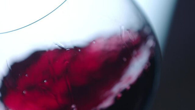 Waving red wine in a glass on defocused background . Beautiful stock footage for wine commercial . Close up video of wine mixing process inside goblet . Shot on ARRI ALEXA Camera in Slow Motion .