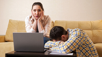 Young stressed family couple tries to calculate high payments on laptop near beige comfortable...