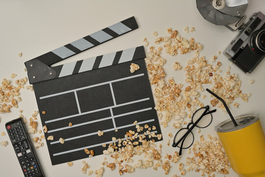 Above view with popcorn spilled on the table and clapper board, remote, eyeglasses, vintage camera and yellow glass decorated.