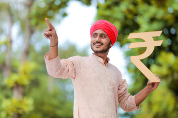 Young indian farmer holding rupees symbol in hand.
