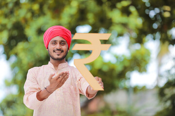 Young indian farmer holding rupees symbol in hand.