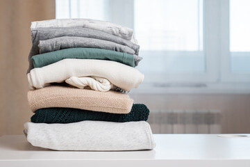 stack of sweater on white table against large window in brightly lit room closeup