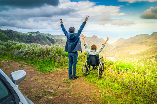 Young man and his wife in wheelchair travelling together by car in mountains