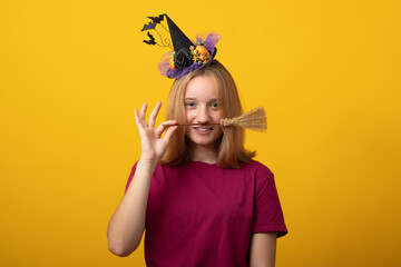Halloween party girl. Happy Halloween witch with a black hat. Beautiful young smiling woman in witches hat and costume on yellow background.