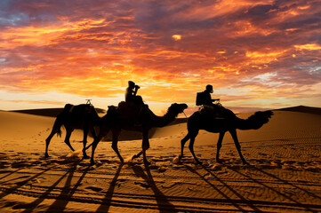 (Selective focus) Stunning sunset behind the silhouette of two tourists riding two camels on the...