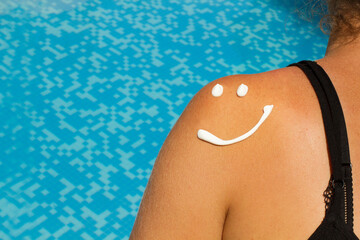 Mujer con protector solar en forma de sonrisa en la espalda junto a una piscina. Vista de frente y...