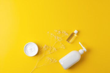 Cosmetic skin care products with flowers on yellow background. Flat lay, copy space