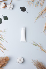 White tube of cosmetic cream with flowers on grey background. Flat lay