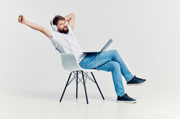 man in white t-shirt sitting on a chair with a laptop in headphones
