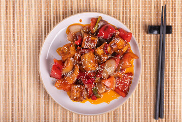 A serving of Korean hot sweet and sour tofu with pepper and onions in a hot sauce with sesame seeds.