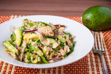 Delicious salad with avocado and canned tuna with onions on a plate, close-up