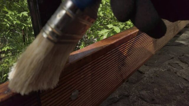 Hand in glove painting fence of impregnated ship floor planks. Carpenter applying protective layer of varnish.
