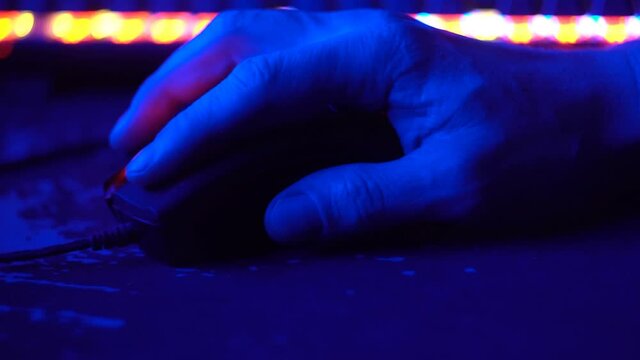 This stock video shows the computer mouse of a player during a gaming session. The room is dark and reflects the dim colored light of gaming hardware.