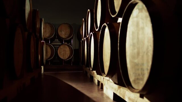 Aged wooden barrels with a wine , brandy or whiskey in a big warehouse . Dolly , gimbal movement a long row of wine barrels at a vintage winery with alcohol . Wine preparation and fermenting process