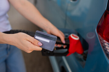 A woman fills her car with gasoline at a self-service gas station and holds a credit card