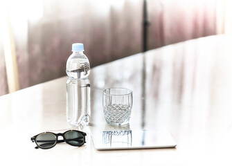 Bottle of water, empty glass, sunglasses and a digital tablet on the office table