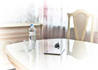 Bottle of water, empty glass, sunglasses and a digital tablet on the table at home
