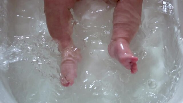 Bathing a newborn. Baby bath time. Unrecognizable baby. Legs only. 5x slow motion.