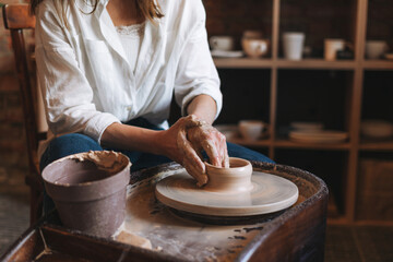 Young attractive woman in white shirt ceramic artist working on potter's wheel in studio. Handmade work student, freelance small business, hobbies and crafting