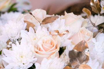 Bridal wedding rings on a bouquet in gold colors with cream roses and daisies