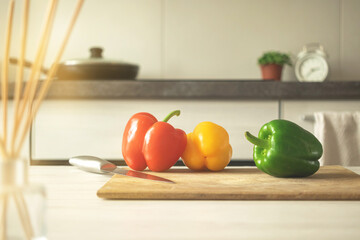 Cutting board with red, yellow and green sweet bell peppers on a modern kitchen background. Vegetable ingredient, cooking healthy food concept