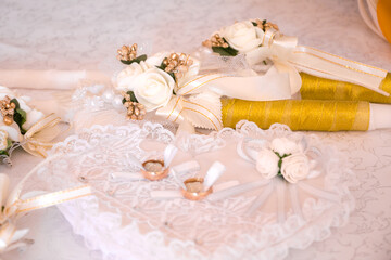 Bridal wedding rings on a white pillow in the shape of a heart. Wedding candles in gold color