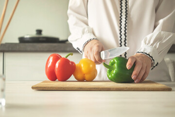 Chef slicing sweet pepper on wooden board, modern kitchen background. Woman chef cooking with ripe vegetable. healthy food concept photo