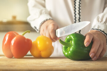 Chef cooking with sweet peppers on wooden board in modern kitchen background. Healthy food concept