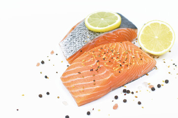 Fresh salmon fillet decorated with black pepper, pink Himalayan salt and lemon on a white background.